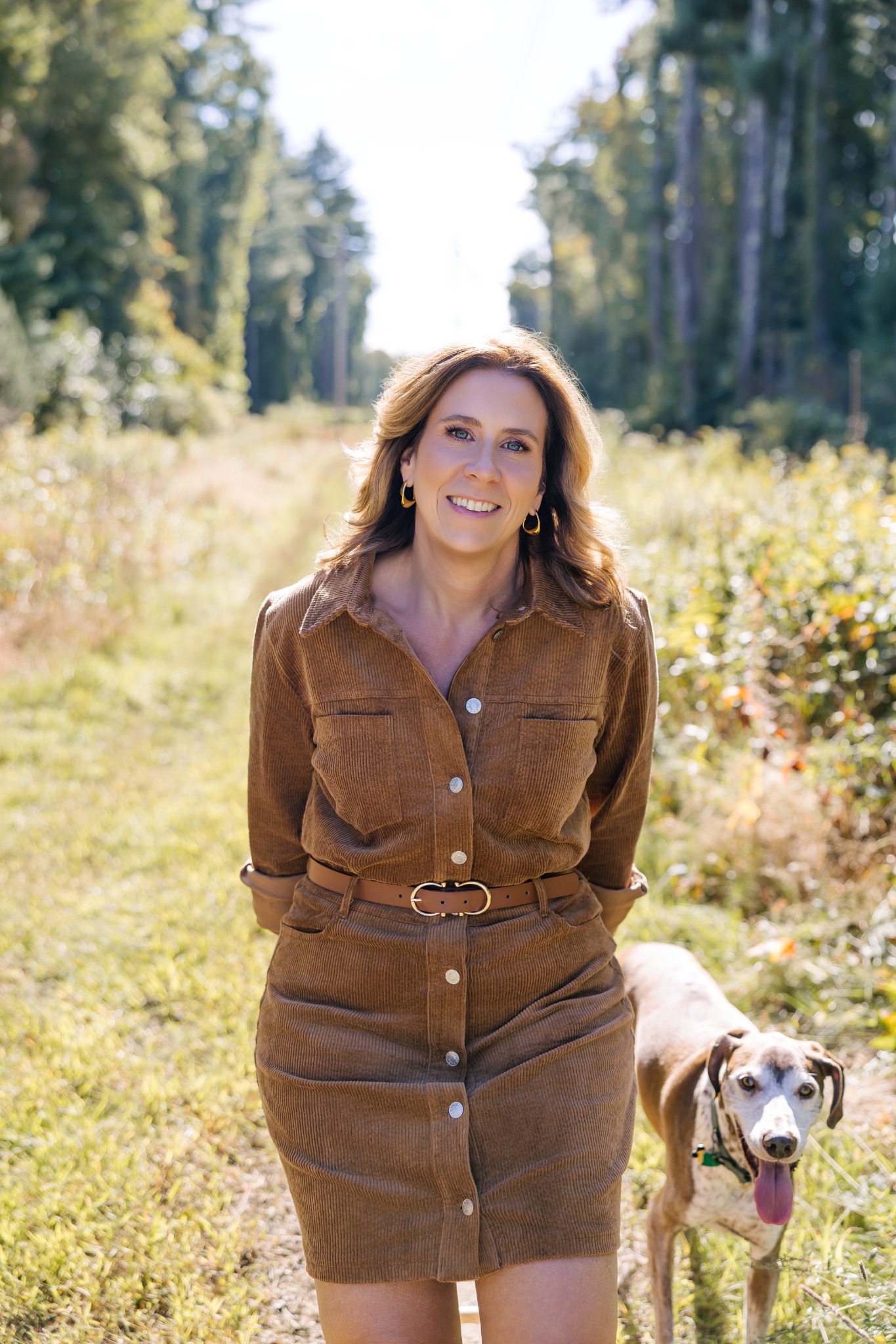 Laura Crosby standing on a sunlit wooded path with her dog